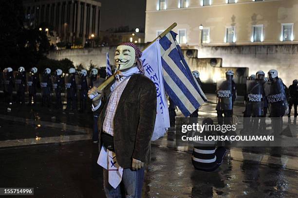 Protester with a Guy Fawkes mask stands in front of riot police near the Greek parliament during a demonstration marking the second day of the...