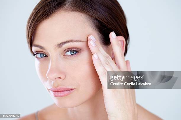 woman touching eye wrinkles with her finger - women wrinkle stockfoto's en -beelden