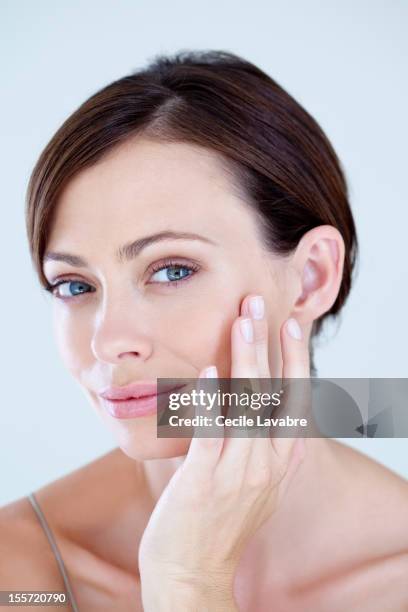 a woman examining her face with her finger - kin in de hand stockfoto's en -beelden