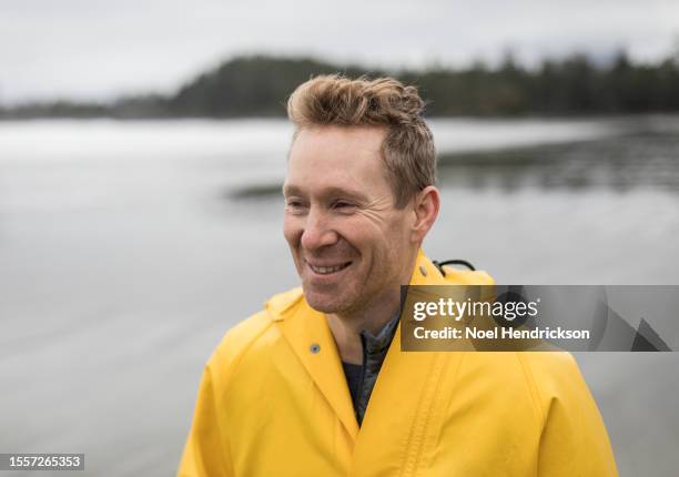 man smiling on beach wearing yellow rainjacket - mature man smiling 40 44 years blond hair stock pictures, royalty-free photos & images