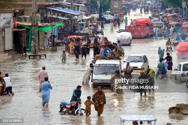 Commuters wade through a flooded street after heavy monsoon rains in Jaffarabad district of Balochistan province on July 27, 2023. Hundreds of people...