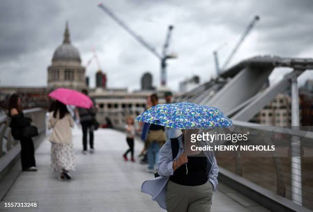 Pedestrians shelter from the rain beneath an umbrella as they walk across the Millennium Bridge, crossing the River Thames, backdropped by St Paul's...