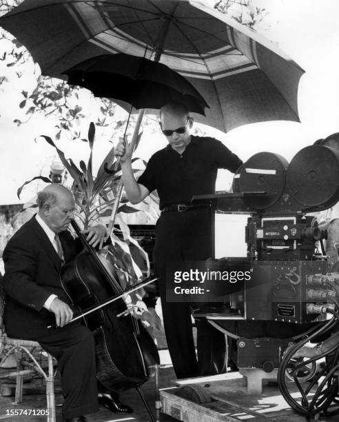 Photo taken 03 August 1957 of Pablo Casals at the age of 80 playing violoncello while his producer Lothar Wolff holds an umbrella to protect him from...