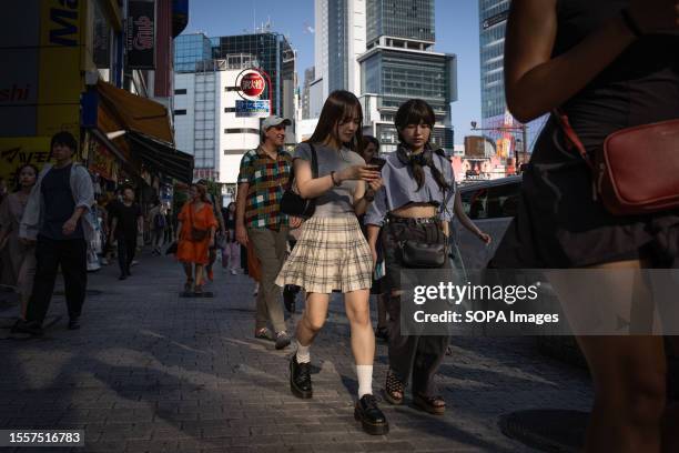 Pedestrians dressed in summer fashion walk on a sidewalk in Shibuya district on a sunny day, when temperatures reached over 36 degrees celsius in...