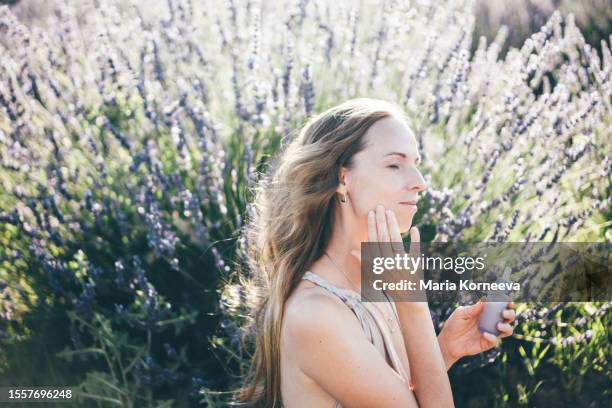 woman using natural essential oil in a lavender field. - schoonheidsspecialist natuur stockfoto's en -beelden