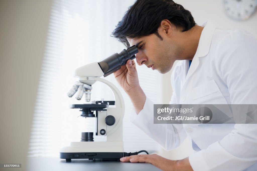 Mixed race scientist peering into microscope