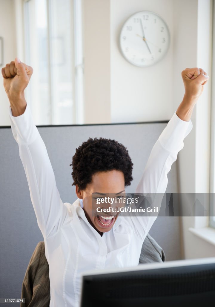 African American businesswoman sitting at desk cheering