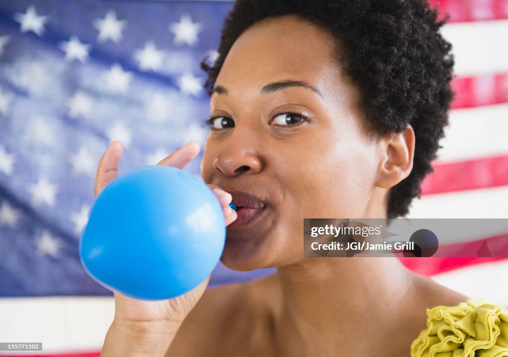 African American woman blowing up blue balloon