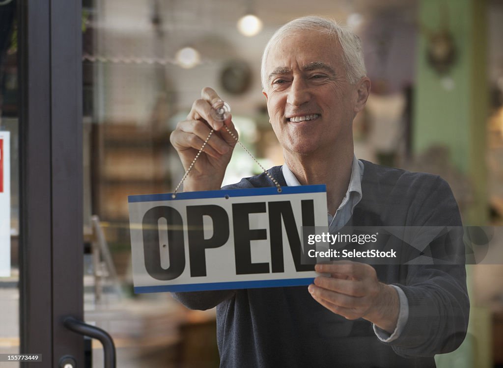 Senior man hanging open sign