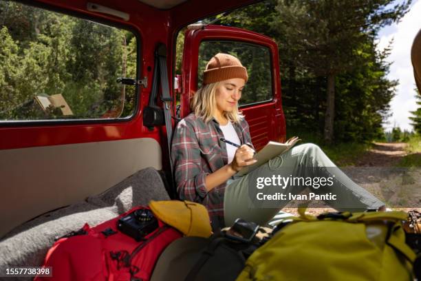 young smiling female tourist taking notes while relaxing on a break in her van. - car break pads stock pictures, royalty-free photos & images