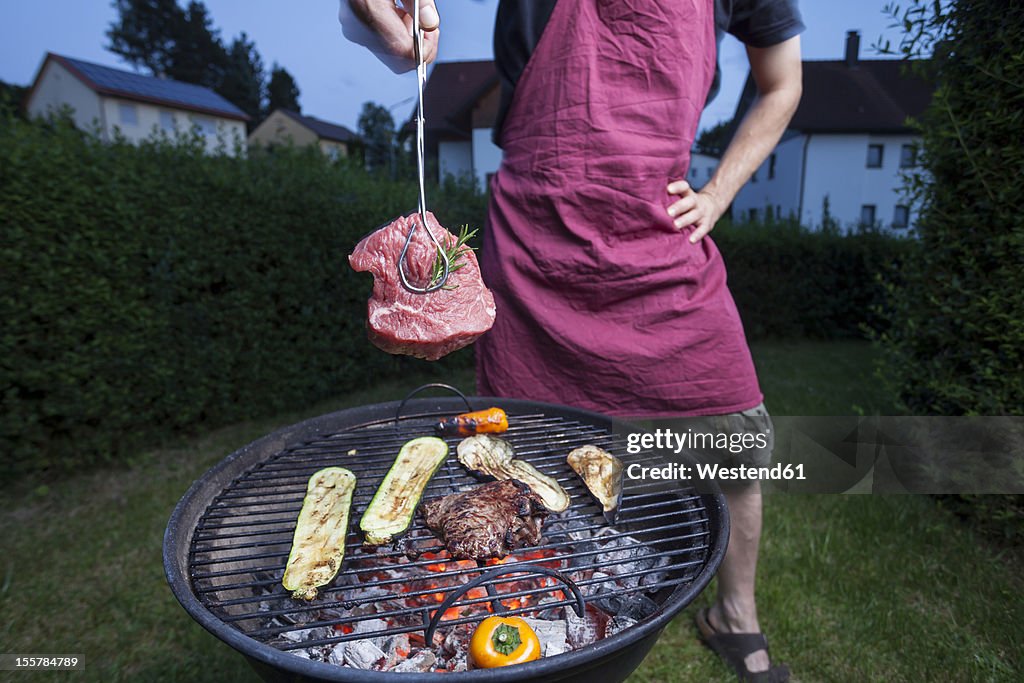 Germany, Bavaria, Mature man holding barbecue on grill with tongs