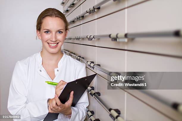 germany, brandenburg, pharmacist with clip board, smiling, portrait - apotheker blick in kamera stock-fotos und bilder