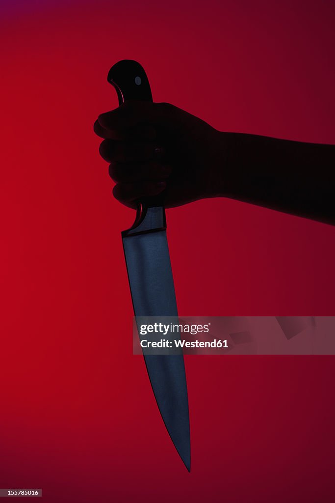 Human hand holding kitchen knife against red background