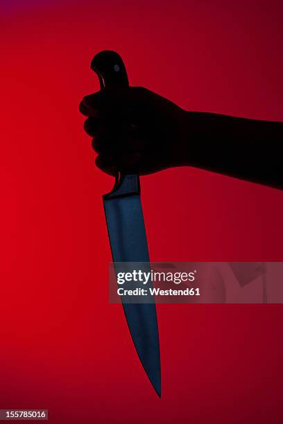 human hand holding kitchen knife against red background - knife weapon stockfoto's en -beelden