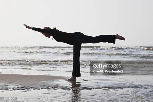 belgium, young woman standing in warrior iii pose at north sea - warrior position stock pictures, royalty-free photos & images