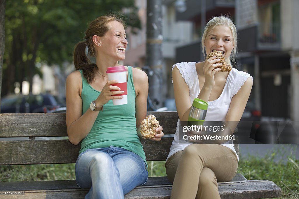 Germany, North Rhine Westphalia, Cologne, Young women sitting on bench with coffee and croissants