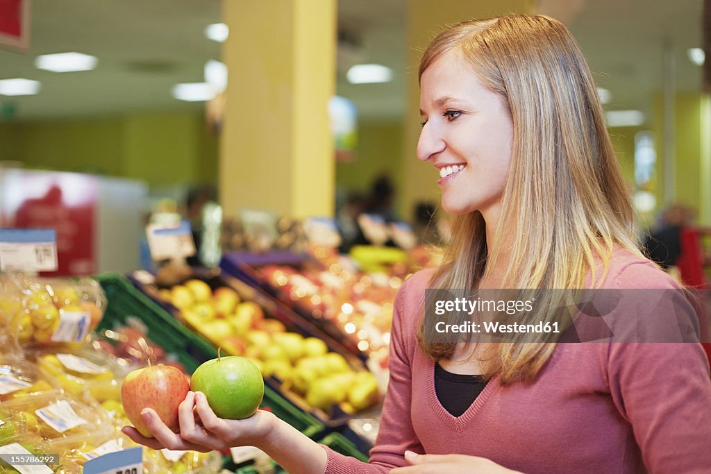 Germany, Cologne, Young woman comparing apples in supermarket