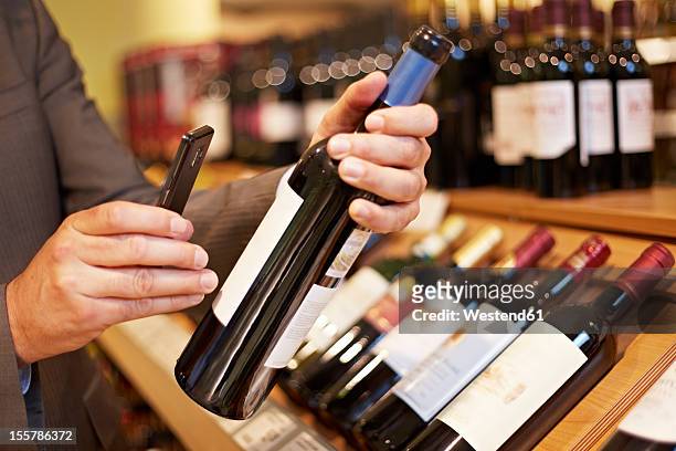 germany, cologne, mature man taking picture of wine bottle in supermarket - cologne label stock pictures, royalty-free photos & images