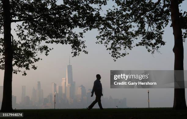 The sun rises on the skyline of lower Manhattan and One World Trade Center in New York City as a man walks through a park on July 20 in Hoboken, New...