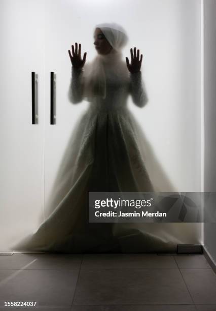 muslim woman in wedding dress standing against glass door - arabic wedding stock pictures, royalty-free photos & images