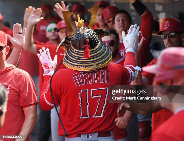 Shohei Ohtani of the Los Angeles Angels gets high-fives from teammates in the dugout while wearing a samurai Kabuto helmet after hitting a home run...