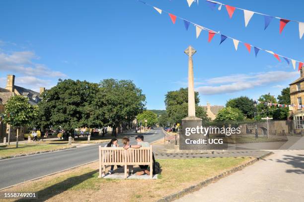 The picturesque Cotswolds village of Broadway in the English county of Worcestershire on a sunny summer's afternoon with young people chatting on a...