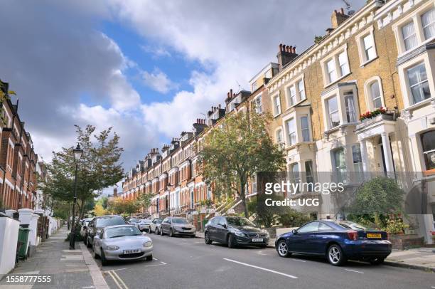 Victorian terraced houses line a residential street with rowan trees in the affluent leafy neighborhood of Hampstead Village in north London.