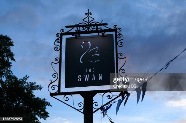 An ornate black metal sign at dusk outside The Swan, a modern pub and restaurant in the Cotswold village of Broadway in Worcestershire, England, UK .