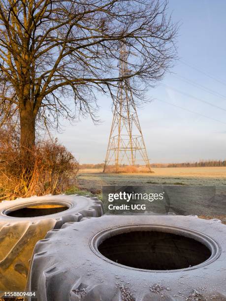 Electricity pylon in a field in Lower Radley Village, footpath blocked by giant tractor tires, winter sunrise.