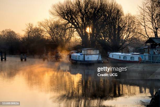 View from Abingdon Weir upstream of the River Thames, misty Autumn sunrise with houseboats.