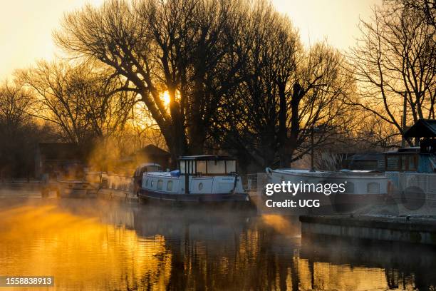View from Abingdon Weir upstream of the River Thames, misty Autumn sunrise with houseboats.