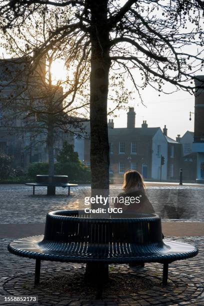 Seated woman in Abingdon Market Place, early winter morning.
