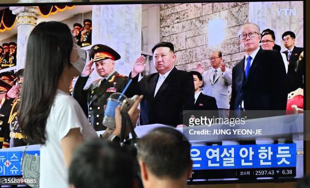 Woman walks past a television screen showing a news broadcast with an image of North Korean leader Kim Jong Un attending a military parade held in...