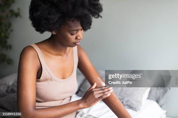 mujer negra adulta joven aplicando crema para la piel en casa por la mañana - untar fotografías e imágenes de stock
