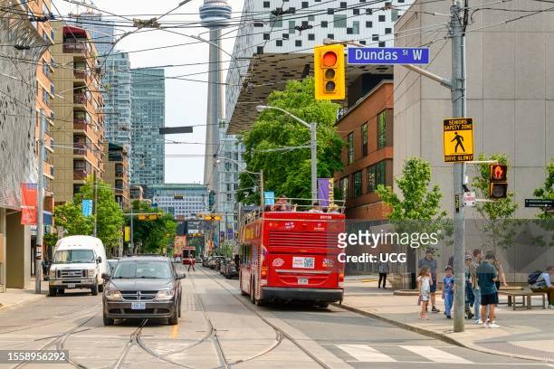 Toronto, Canada, A red open roof tour bus with passengers on Dundas St W. The CN tower is visible in the background.