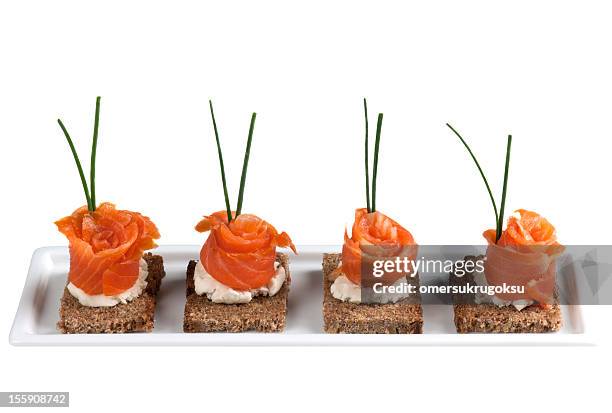 a row of garnished salmon canapes on a white platter - canape stock pictures, royalty-free photos & images