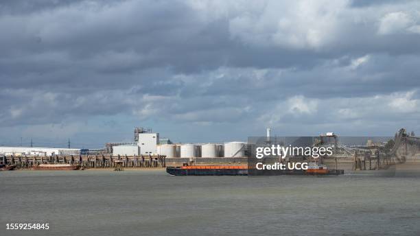 Dry elevator hopper barge KG17 is pushed upstream by a tug on the River Thames by the oil storage depot at Purfleet in Essex and the Dartford...