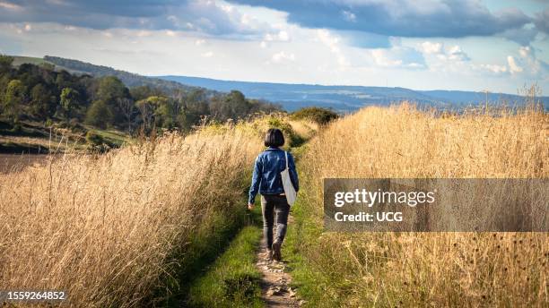 Women carrying a bag walks along the South Downs Way long distance path in West Sussex, UK.