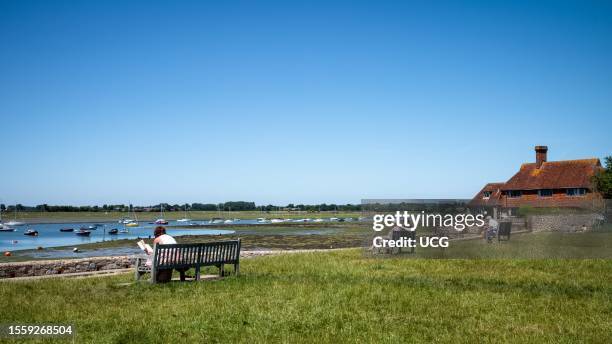 People sit on benches overlooking Chichester Harbor at Bosham in West Sussex, UK.