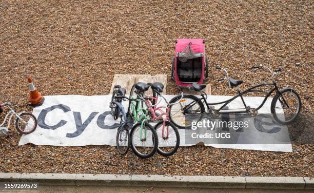 Large sign saying "Cycle Hire" and various bicycles for hire on the beach at Brighton, East Sussex, UK. The bikes include a tandem and children's...