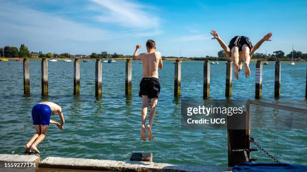 Three teenage boys ready themselves to dive into the sea at high tide at Bosham, West Sussex, UK.