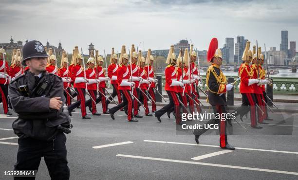 Policeman stands guard as soldiers from the British Army's Household Cavalry Life Guards Regiment bear their swords and wearing full dress uniform...