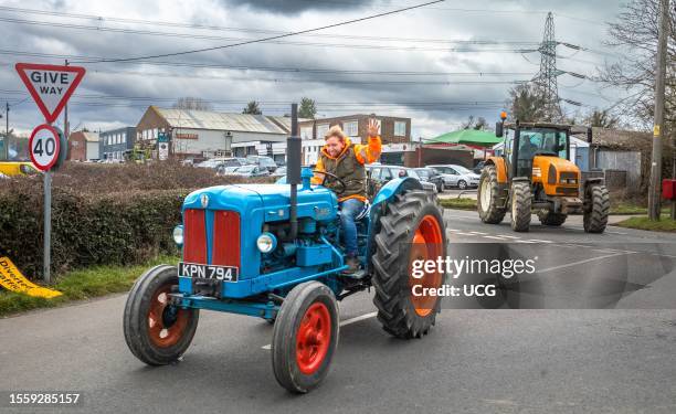 Participant in a charity tractor parade waves as he turns a corner in his vintage Fordson Major on a country lane in West Sussex, UK.