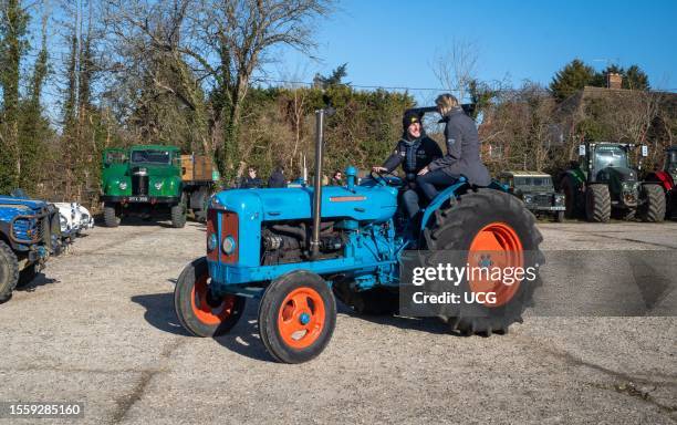 Man driving a vintage Fordson tractor looks at his partner sitting on the wheel arch at a vintage tractor rally in Wisborough Green, UK.