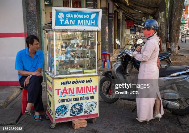 Man waits as a watch repairer fixes his watch, while a female customer has just arrived at the stall in the Central Market in Kontum, in the Central...