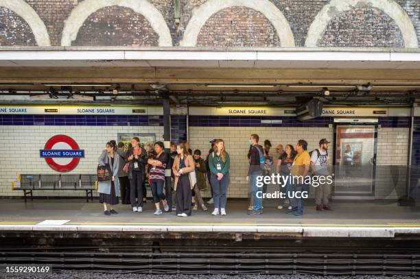 Group of people wait for an underground train on the platform at Sloane Square tube station in London.