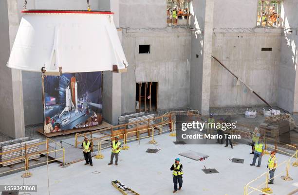 Workers look on as the first of two aft skirts from the Space Shuttle Endeavour is lowered onto the seismic isolation pad during the first...