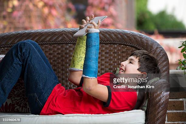 boy with two broken arms enjoys time on a tablet. - boy broken arm stock pictures, royalty-free photos & images