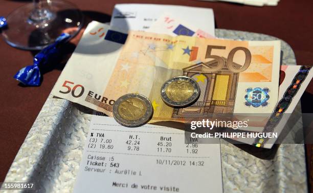 Picture taken on November 10, 2012 in a restaurant in Lille shows euro coins and bank notes set up on a bill with the 19,60 percent value added tax ,...