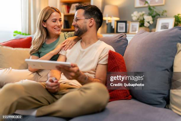 husband showing something on the digital tablet to his wife at home - couple choosing stock pictures, royalty-free photos & images